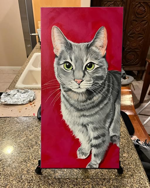 Painting of a grey tabby cat on a red background, on the easel